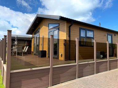 A modern wooden lodge with glass railing on the deck and outdoor dining furniture at Lodge 18 - The Pines in Runswick Bay