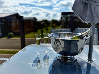 An outdoor glass table with a champagne bottle in an ice bucket and two filled champagne glasses at Lodge 18 - The Pines in Runswick Bay