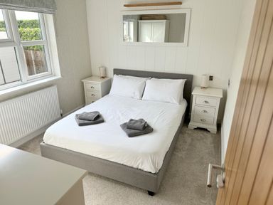 A bedroom with a bed with white sheets and pillows and two folded towels on top with two bedside tables and lamps and a mirror on the wall at Lodge 18 - The Pines Runswick Bay