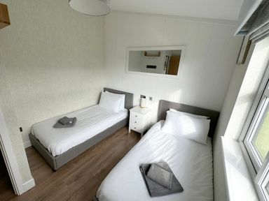 A bedroom with two single beds a small white nightstand and a window at Lodge 18 - The Pines in Runswick Bay
