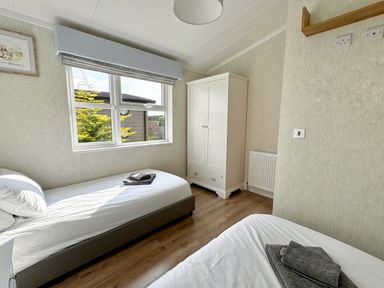 A bedroom with two single beds a white wardrobe a window and wooden flooring at Lodge 18 - The Pines in Runswick Bay