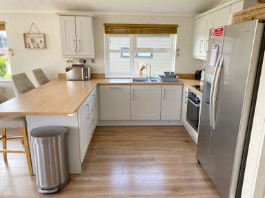 A kitchen with wooden countertops white cabinets a stainless steel refrigerator a microwave and chairs at Lodge 18 - The Pines in Runswick Bay