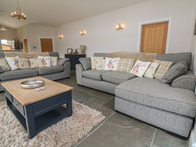 A living room with two gray sofas with patterned cushions a wooden coffee table on a rug and wooden doors at Silver Birch in Dolton
