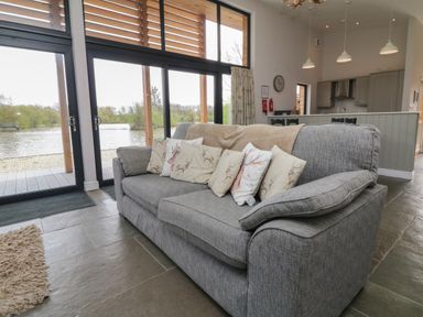 A living room with a gray sofa and cushions next to large glass sliding doors overlooking a lake at Silver Birch in Dolton
