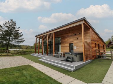 A wooden house with an outdoor seating area and hot tub next to a grassy yard and a tree at Silver Birch in Dolton