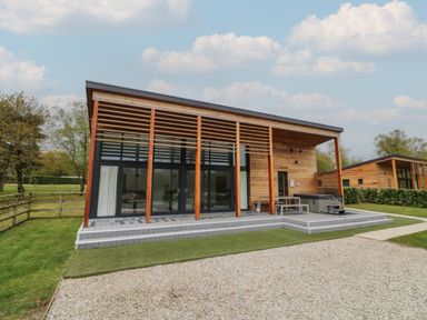 A modern wooden house with large glass doors and a patio with a hot tub and seating at Silver Birch in Dolton