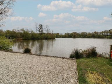 A gravel area next to a lake with trees and bushes at Silver Birch in Dolton