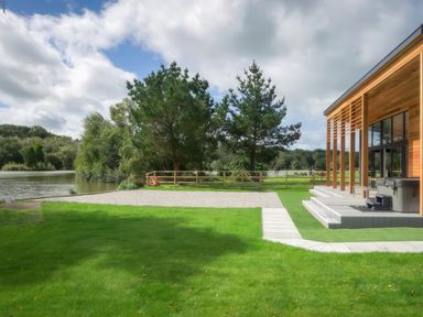 A lawn with a wooden modern building on the right and a lake with trees in the background at Silver Birch in Dolton