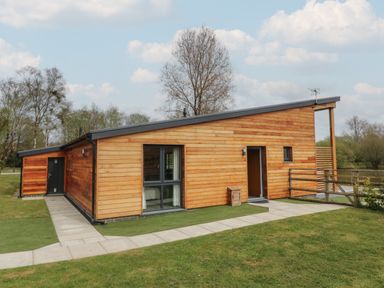 A wooden house with large windows and a paved walkway surrounded by grass and trees at Cherry in Dolton