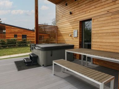 An outdoor deck with a hot tub and a picnic table next to a wooden building at Cherry in Dolton