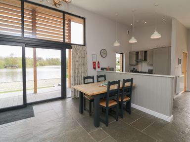 A dining area with wooden table and chairs next to large glass doors overlooking a lake at Cherry in Dolton