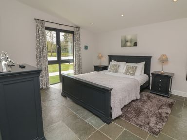 A bedroom with a double bed bedside tables lamps a dresser and large windows with curtains at Cherry in Dolton