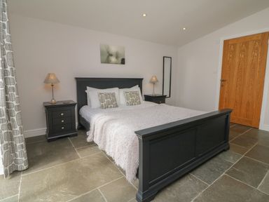 A bedroom with a black bed frame two bedside tables with lamps a wooden door and a floor mirror at Cherry in Dolton