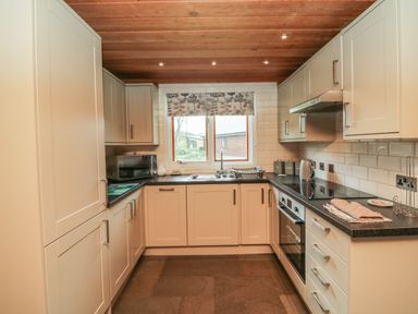 A kitchen with white cabinets black countertops a window with a patterned blind a microwave kettle and built in oven at Aspen in Dolton