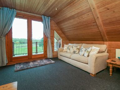 A living room with a beige sofa with cushions next to wooden walls and a glass door with curtains at Aspen in Dolton
