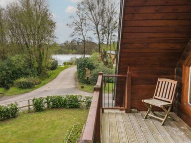 A wooden balcony with a chair overlooking a path and trees near a lake at Aspen in Dolton