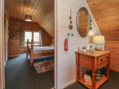 A bedroom with a wooden bed and dresser and a hall area with a wooden table mirror and lamp at Aspen in Dolton