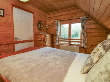 A bedroom with a wooden bed chest of drawers a window with curtains and a white door at Aspen in Dolton