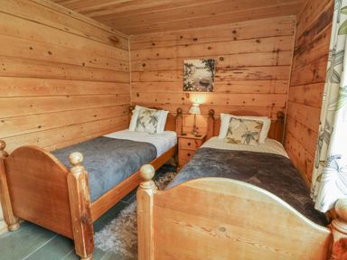 A bedroom with two single wooden beds a bedside table with a lamp and a painting on the wooden wall at Aspen in Dolton