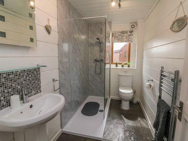 A bathroom with a shower, toilet, sink, mirror, towel rack, and window at Aspen in Dolton