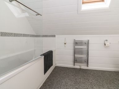 A bathroom with a bathtub a black towel a wall-mounted heated towel rail and a window at Aspen in Dolton