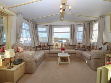 A living room with a corner sofa a coffee table a lamp and multiple windows at Tir Glyn Caravan in Uwch Mynydd near Aberdaron