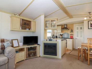 A living room with a television sofa dining table and kitchen area at Tir Glyn Caravan in Uwch Mynydd near Aberdaron