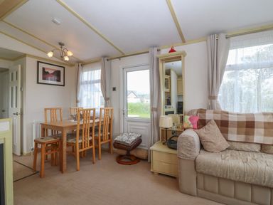 A dining area with wooden table and chairs next to a beige sofa and side table at Tir Glyn Caravan in Uwch Mynydd near Aberdaron