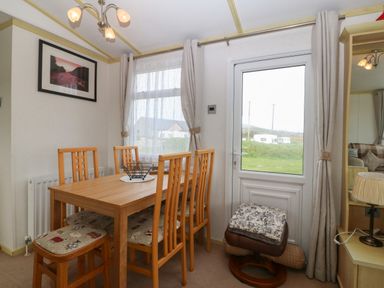 A dining area with a wooden table and four chairs near a window and door at Tir Glyn Caravan in Uwch Mynydd near Aberdaron