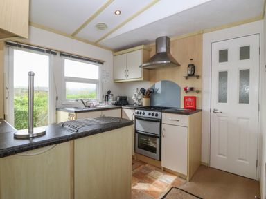 A kitchen with stove microwave and cabinets near a window and door at Tir Glyn Caravan Uwch Mynydd near Aberdaron