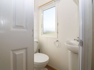 A bathroom with a toilet sink window and door at Tir Glyn Caravan in Uwch Mynydd near Aberdaron