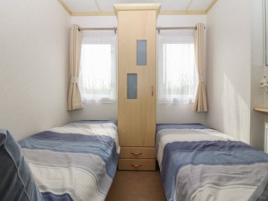 A bedroom with two single beds separated by a wardrobe and two windows with curtains at Tir Glyn Caravan in Uwch Mynydd near Aberdaron