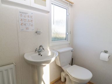 A bathroom with a sink and toilet next to a window at Tir Glyn Caravan in Uwch Mynydd near Aberdaron