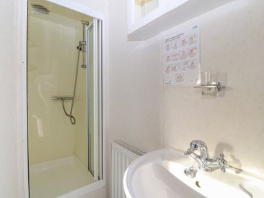 A bathroom with a shower area, a sink with chrome faucets, a glass holder, and a hand-washing technique poster on the wall at Tir Glyn Caravan in Uwch Mynydd near Aberdaron