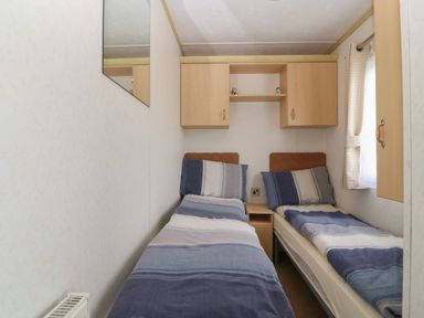 A small bedroom with two single beds with blue striped bedding and overhead cabinets at Tir Glyn Caravan in Uwch Mynydd near Aberdaron