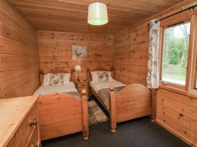 A bedroom with two single wooden beds a nightstand a lamp a window with curtains and a chest of drawers at Maple in Dolton