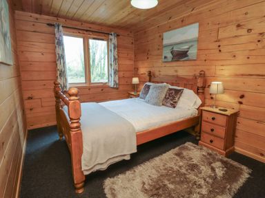 A bedroom with wooden walls and ceiling a bed with pillows two bedside tables with lamps and a window with curtains at Maple in Dolton
