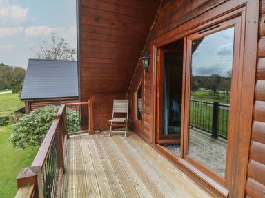 A wooden balcony with a chair and glass door overlooking grass and trees at Cedar in Dolton