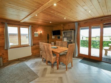 A dining area with a wooden table and six wicker chairs next to windows and glass doors at Cedar in Dolton