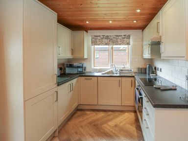 A kitchen with white cabinets a black countertop a stove a microwave a sink under a window and a wooden ceiling at Cedar in Dolton