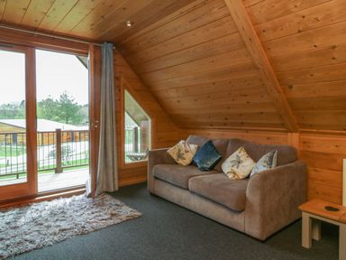 A wooden room with a gray sofa with cushions a small side table and glass doors leading to a balcony at Cedar in Dolton