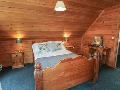 A bedroom with wooden walls a double bed two bedside tables with lamps and a wooden dressing table with a mirror at Cedar in Dolton
