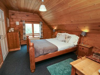 A bedroom with wooden walls and ceiling a bed bedside tables lamps a chest of drawers and a window at Cedar in Dolton