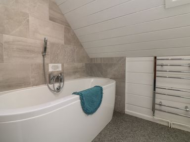 A bathroom with a white bathtub blue towel gray tiled wall and chrome heated towel rail at Willow in Dolton