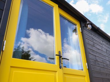 Yellow double doors with glass panels on a black wooden building exterior at Tower Hut in Ryde