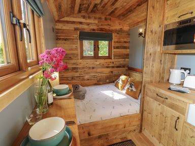 A small wooden room with a bed, kitchen counter, microwave, kettle, bowls, and flowers on a table at Tower Hut in Ryde