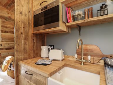 A kitchen countertop with a sink kettle toaster and wooden shelves at Tower Hut in Ryde