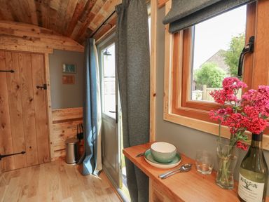 A wooden room with a door window curtains dishes flowers and a wine bottle at Tower Hut in Ryde