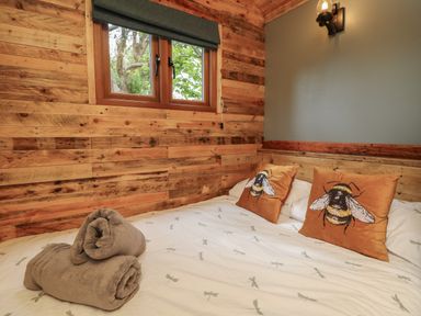 A bedroom with a wooden wall a window two bee patterned pillows on the bed and three rolled towels on the bed at Tower Hut in Ryde