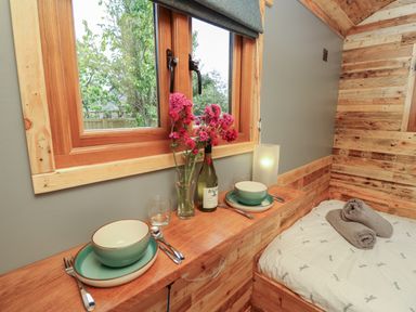 A small wooden dining area with tableware and flowers next to a bed in a wooden cabin at Tower Hut in Ryde